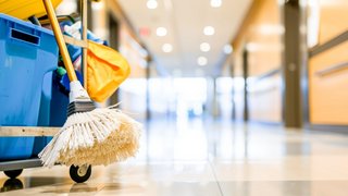 Cleaning cart loaded with a mop and broom stands in the hallway of an office building as background.