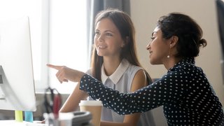 Happy caucasian intern listening to indian mentor explaining computer task
