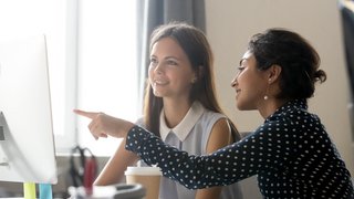 Happy caucasian intern listening to indian mentor explaining computer task
