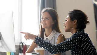 Happy caucasian intern listening to indian mentor explaining computer task
