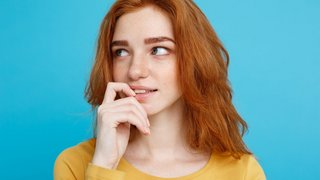 Headshot Portrait of happy ginger red hair girl with freckles smiling looking at camera. Pastel blue background. Copy Space.