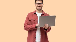 Young man standing holding laptop and looking at camera with happy smile