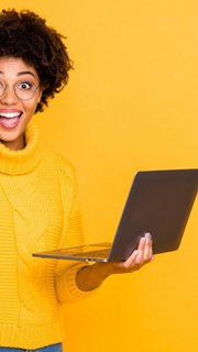 Portrait of her she nice attractive lovely charming smart clever cheerful wavy-haired girl holding in hands laptop celebrating winning isolated over bright vivid shine vibrant yellow color background