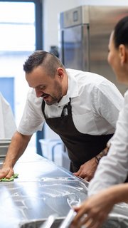Chef and cook cleaning the workspace after doing dishes indoors in restaurant kitchen.