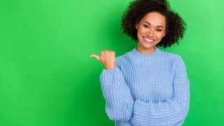 Photo of funny nice girl curly hairstyle wear blue sweater directing empty space promo news sale isolated on green color background