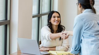 Young adult female business owner shakes hand with unrecognizable client